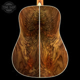 Close-up of the back of an acoustic guitar showing a rich, symmetrical wood grain pattern in warm brown and golden tones, with a white edge trim and a black background. A 'TONE SHOP' watermark is visible in the top left corner.