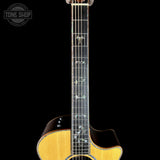 Close-up of an acoustic guitar's neck and lower body against a black background, with a Tone Shop watermark in the upper left corner.
