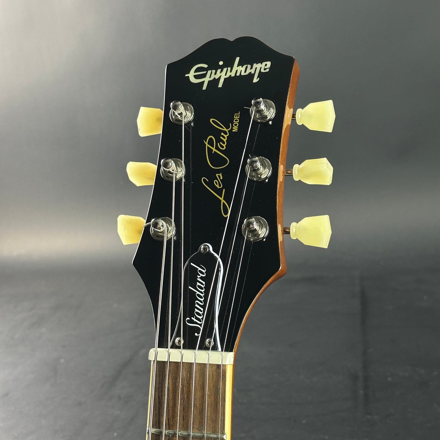 Guitar headstock with 'Epiphone' and 'Les Paul Standard' branding on a gray background
