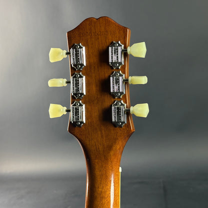 Close-up of a guitar headstock with tuning pegs on a gray background