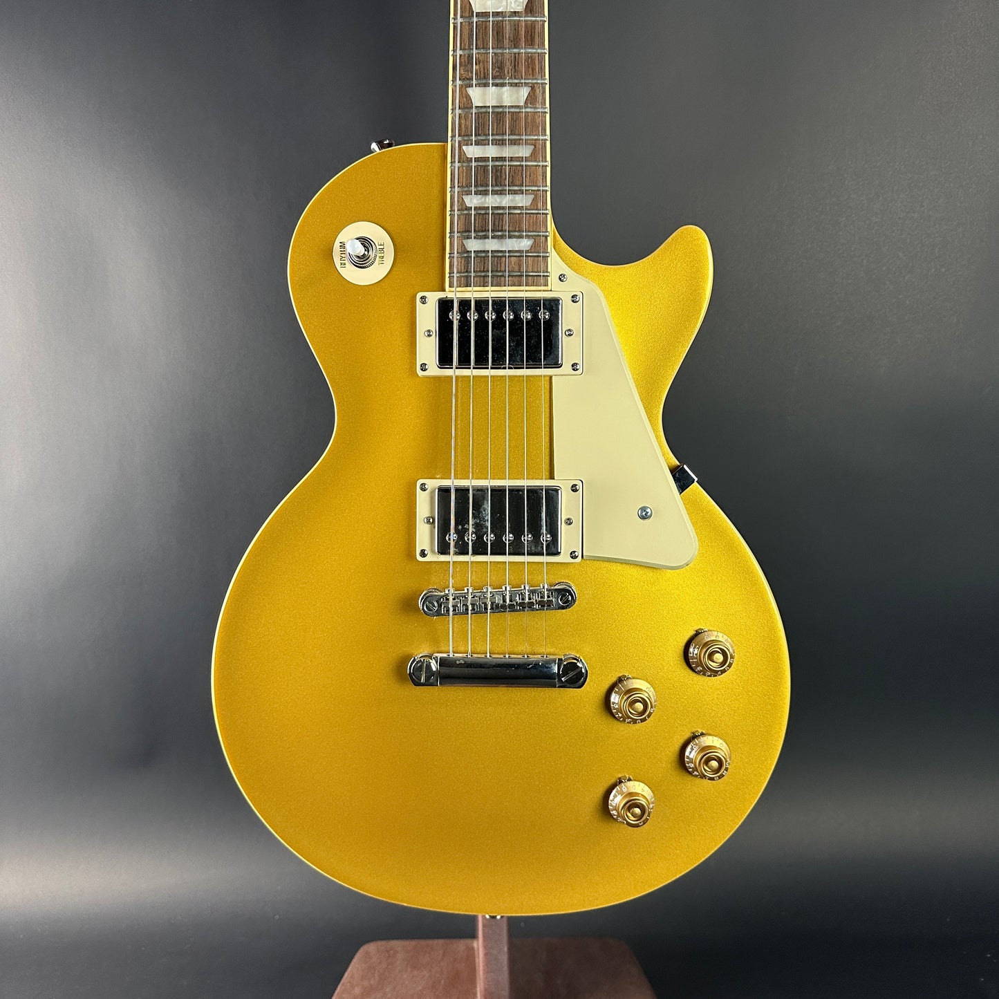 Gold electric guitar on a stand against a gray background