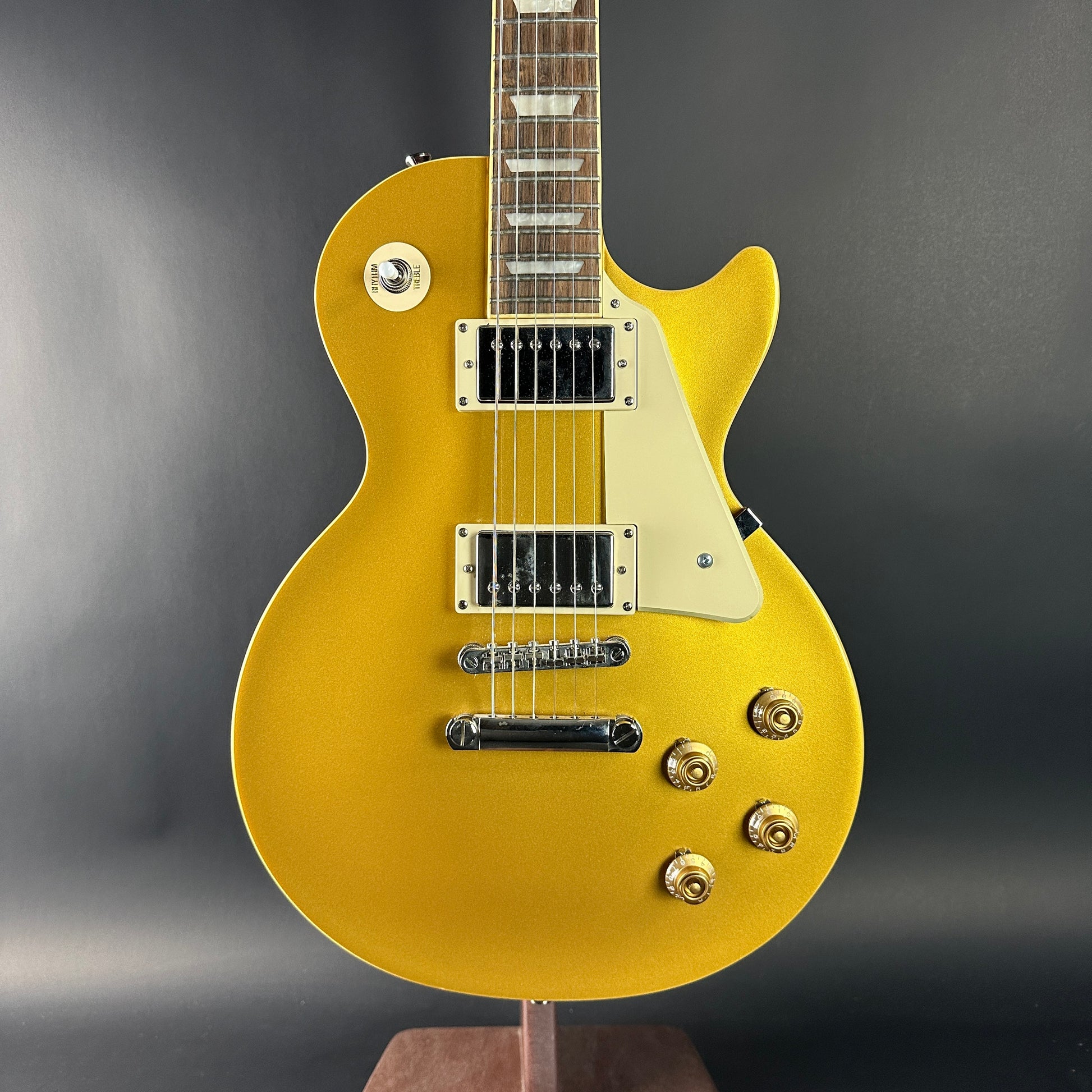 Gold electric guitar on a stand against a gray background