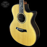 A Taylor acoustic-electric guitar with a natural wood top and dark sides, shown against a solid black background with a Tone Shop watermark in the top left corner.
