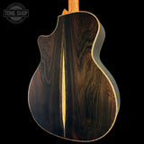 The back of an acoustic guitar made of dark brown wood with a prominent central light wood strip, shown against a solid black background. A 'TONE SHOP' watermark is visible in the top-left corner.