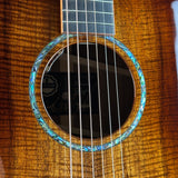 Close-up of a Taylor acoustic guitar body showing the sound hole with a blue abalone shell inlay, rich wood grain, and six strings.