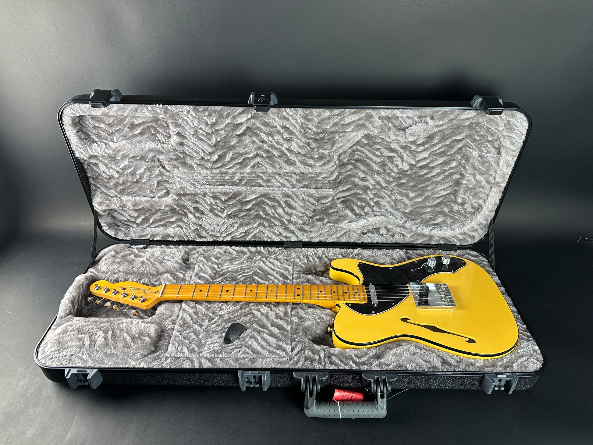 Yellow electric guitar inside an open hard-shell case on a gray background
