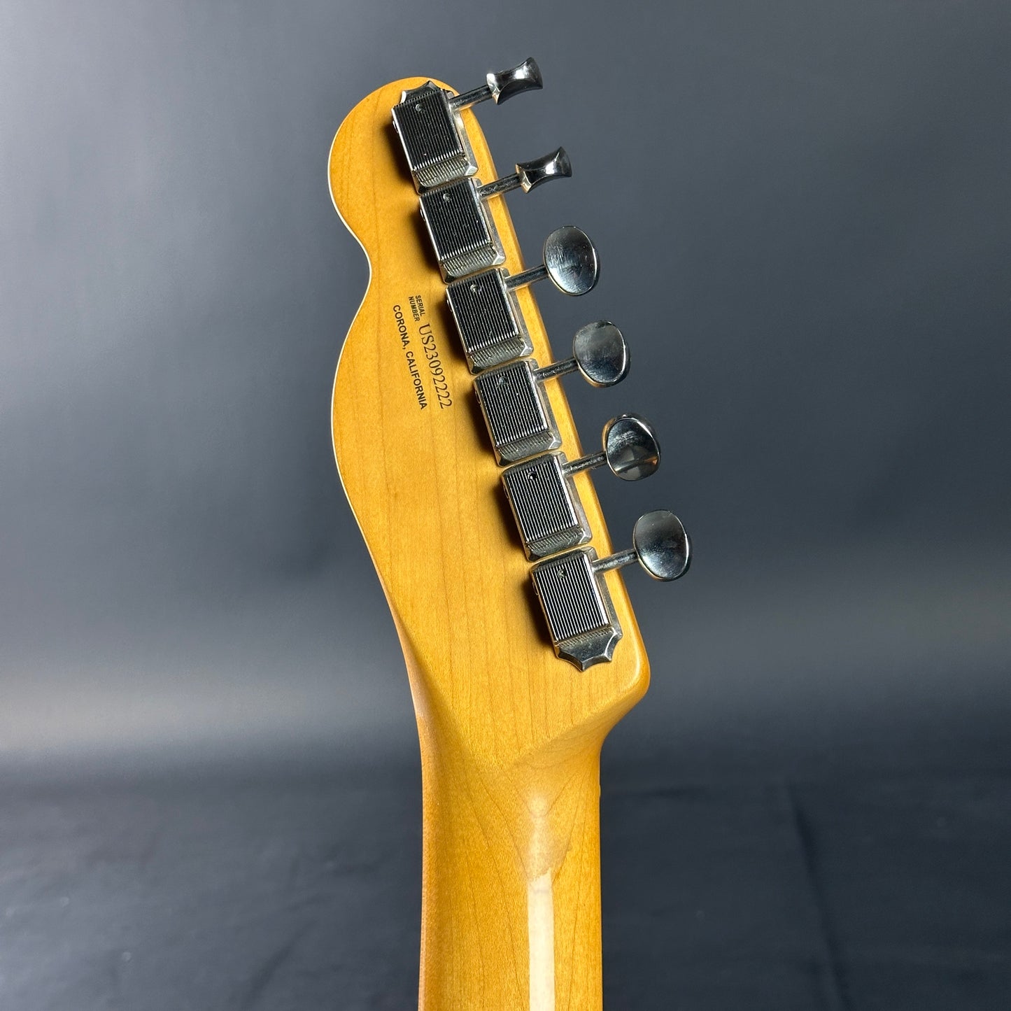 Close-up of a guitar neck with tuning pegs on a dark gray background