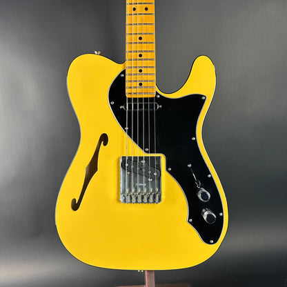 Yellow electric guitar with a black pickguard on a gray background