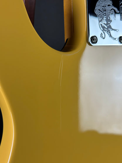 Close-up of a yellow guitar neck with a brand logo on the headstock.