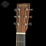 Close-up of the headstock of a Martin & Co acoustic guitar against a black background, showing the brand name in gold script and six silver tuning pegs.