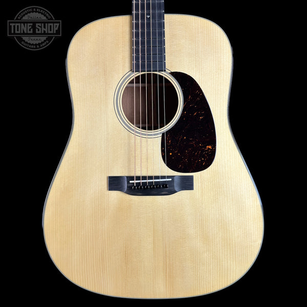 A front-facing acoustic guitar with a natural light wood finish, dark pickguard, and black bridge, shown against a solid black background. A circular 'TONE SHOP' watermark is visible in the top-left corner.