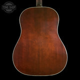 The back of an acoustic guitar with a rich, warm brown wood finish and white binding, shown against a solid black background with a Tone Shop watermark in the top left corner.