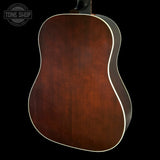The back of an acoustic guitar with a rich, warm brown wood finish and white binding, shown against a solid black background with a Tone Shop watermark in the top left corner.