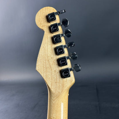 Close-up of a guitar headstock with tuning pegs on a gray background