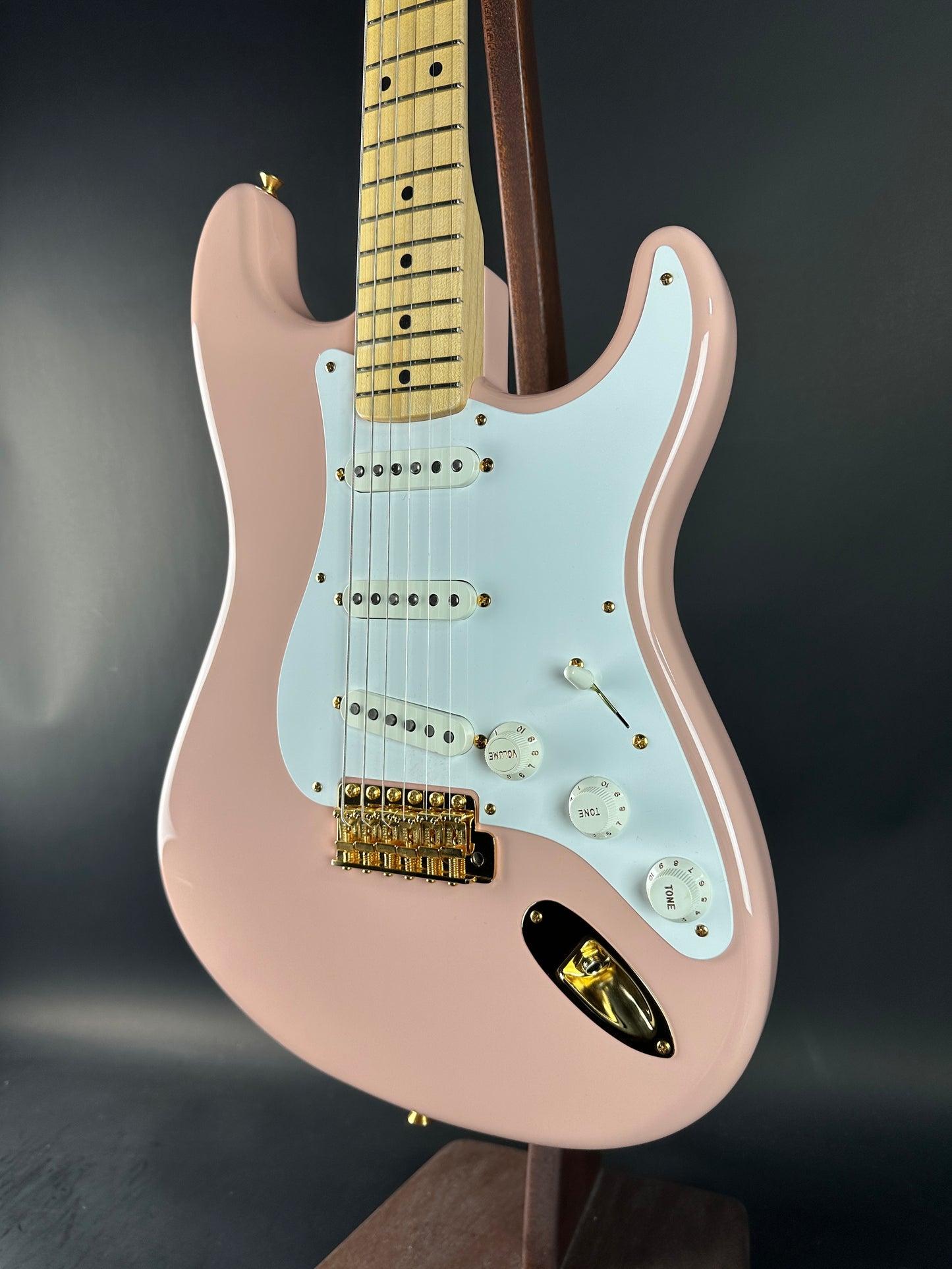 Pink electric guitar with a white pickguard on a dark background