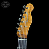 Close-up of the headstock of a Fender Telecaster electric guitar, showing the wood grain, six silver tuning pegs, and the Fender logo, set against a solid black background.