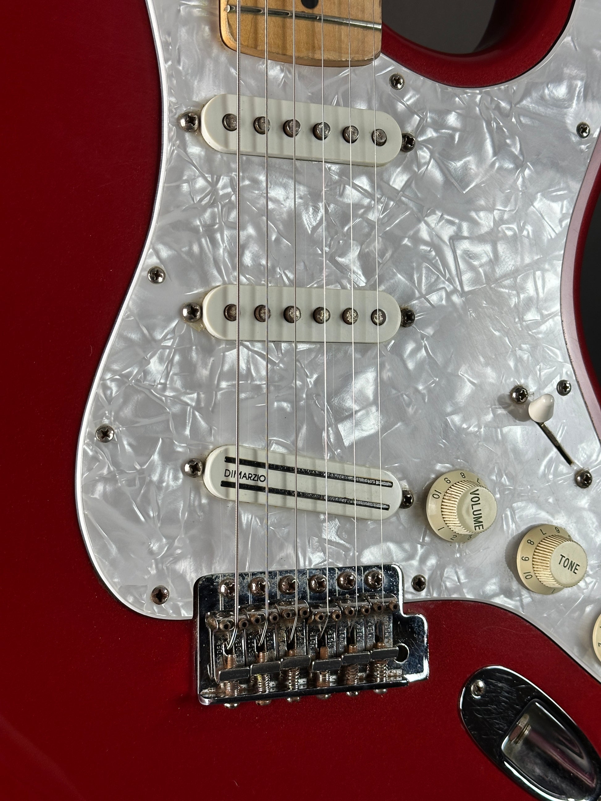Close-up of a red electric guitar with white pickguard and control knobs.