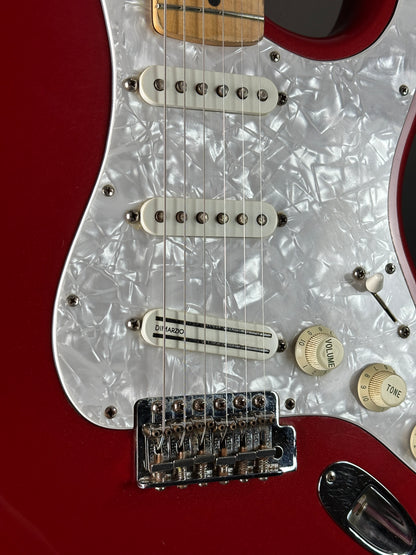 Close-up of a red electric guitar with white pickguard and control knobs.