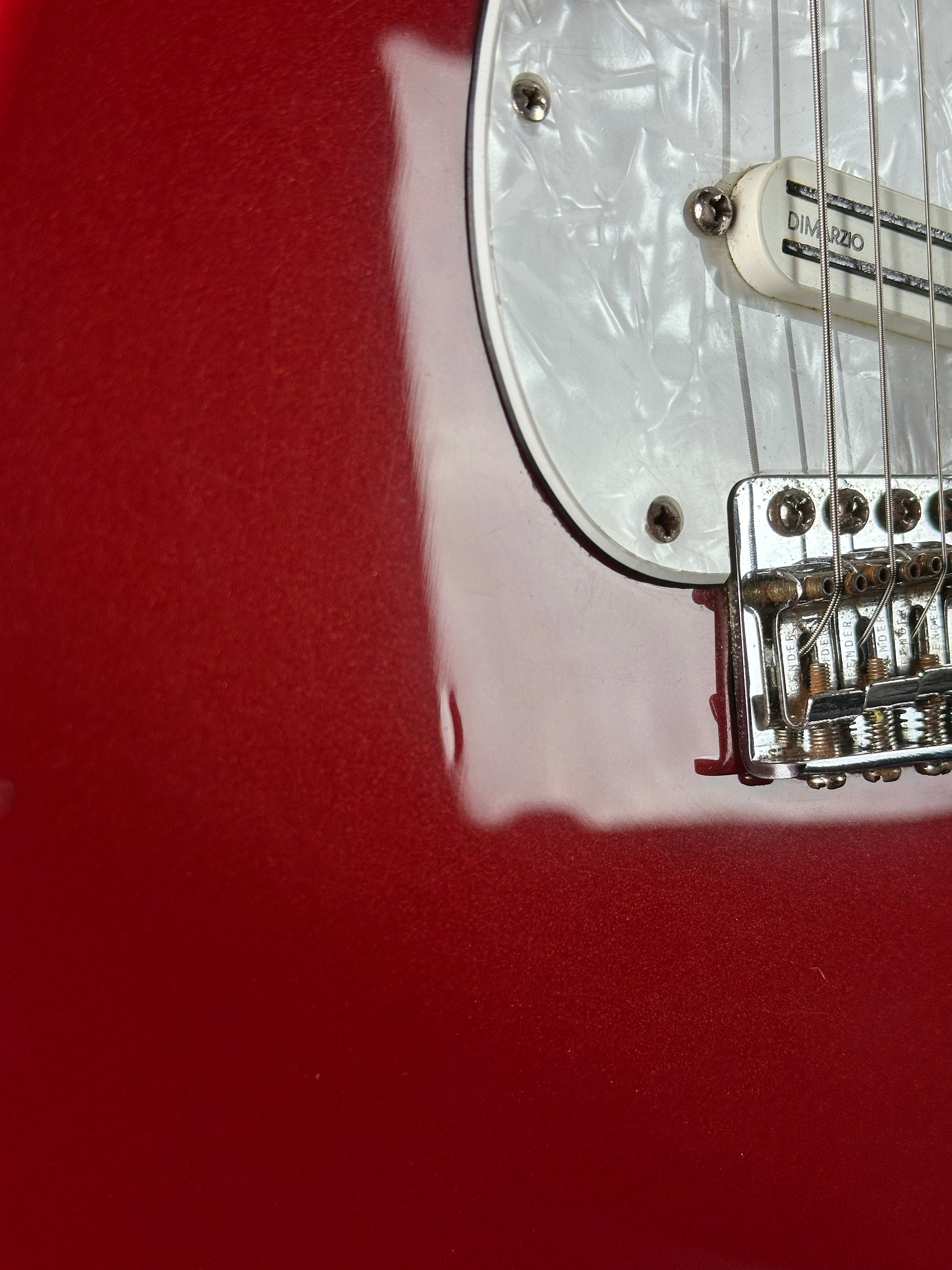 Close-up of a guitar's pickguard and bridge against a red background