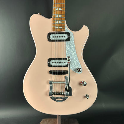 Beige electric guitar with a black pickguard on a dark gray background
