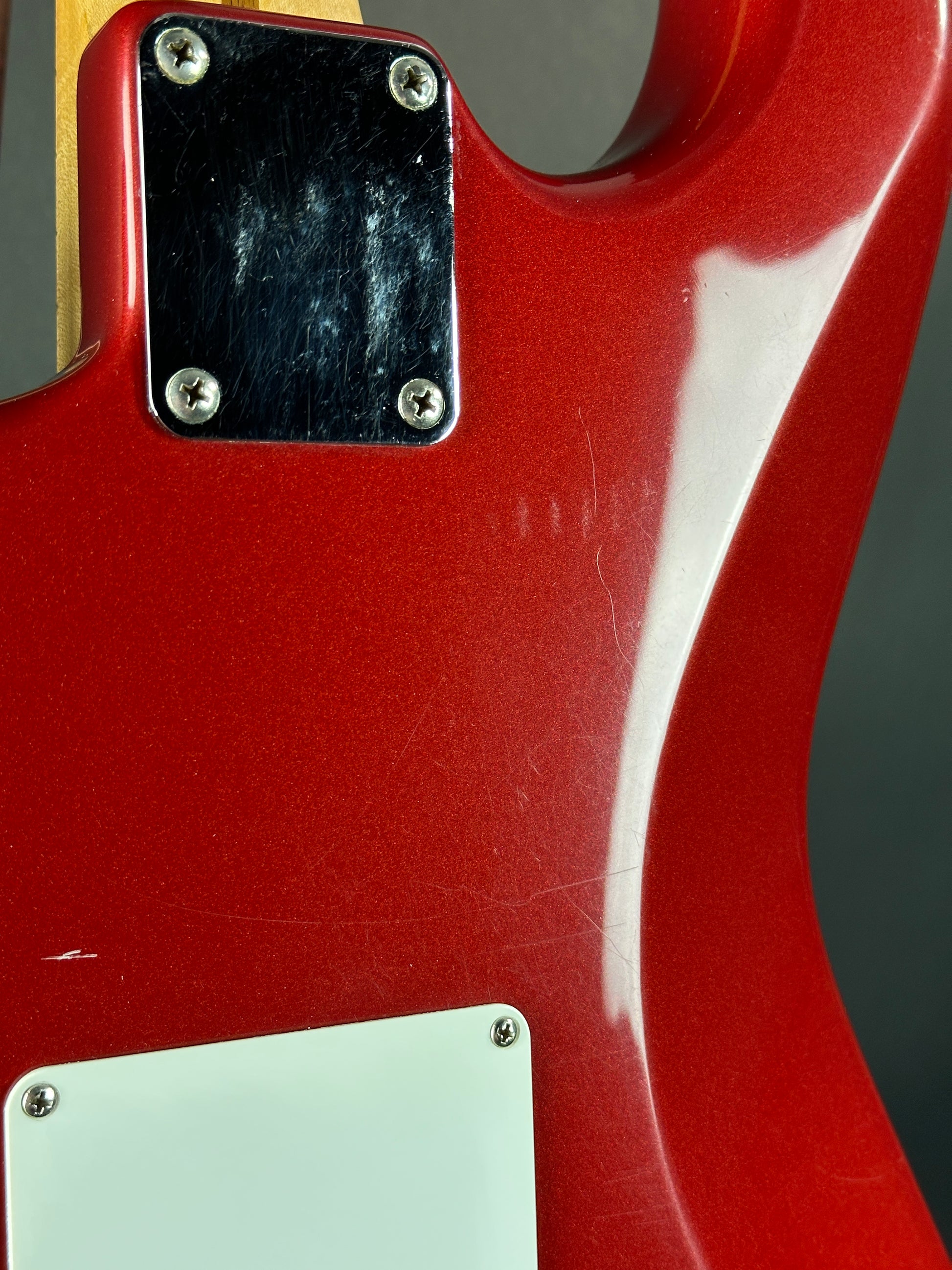 Close-up of a red electric guitar body with a black pickguard and white label.