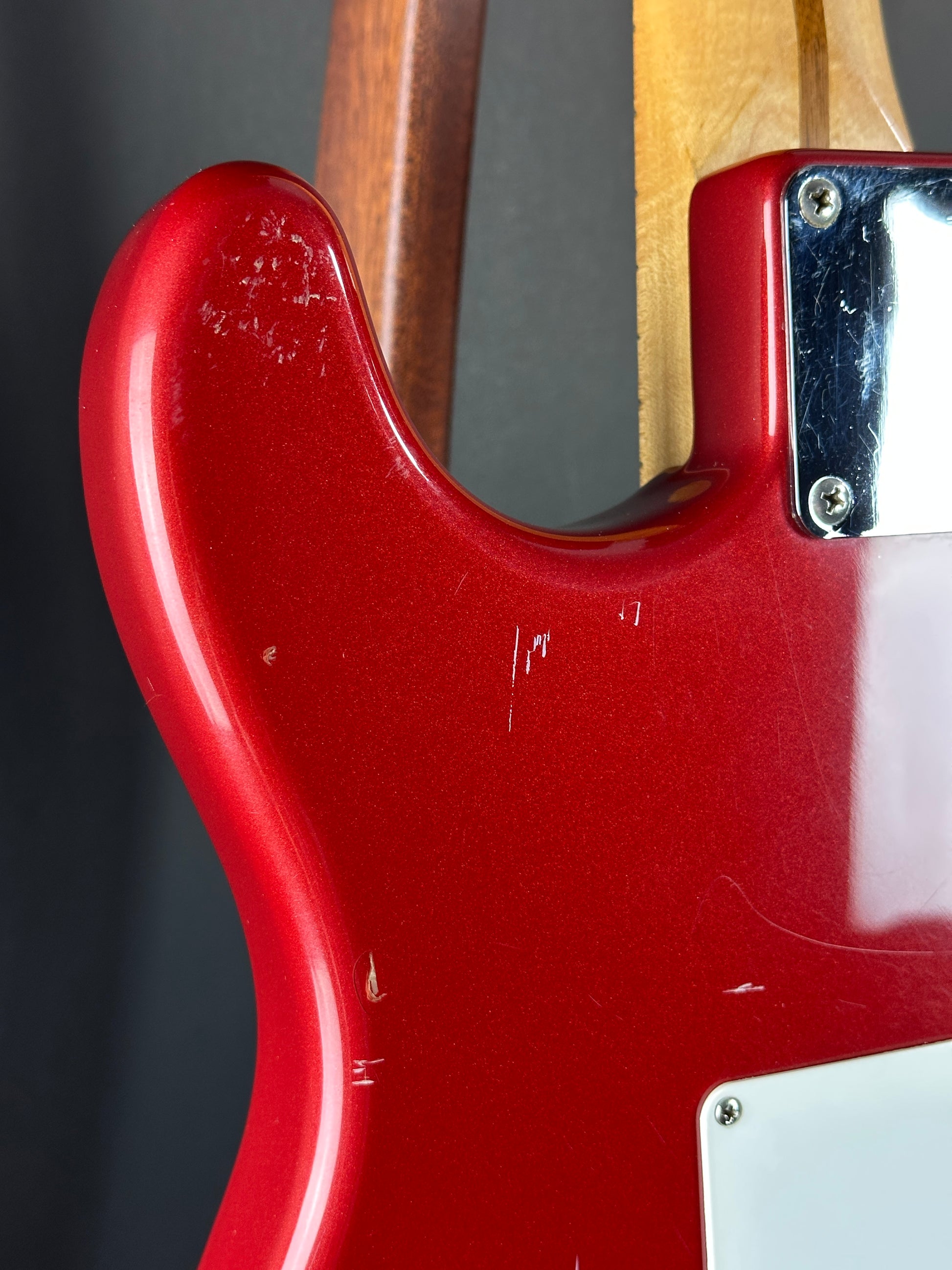 Close-up of a red electric guitar body with a wooden neck.