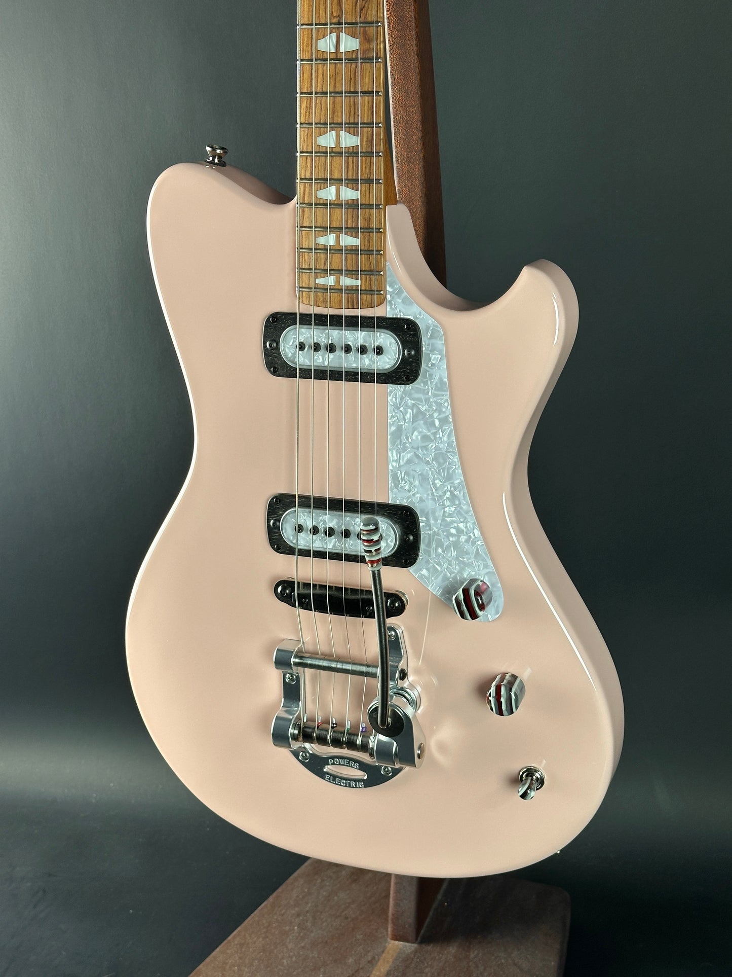 Beige electric guitar with a black pickguard on a dark gray background