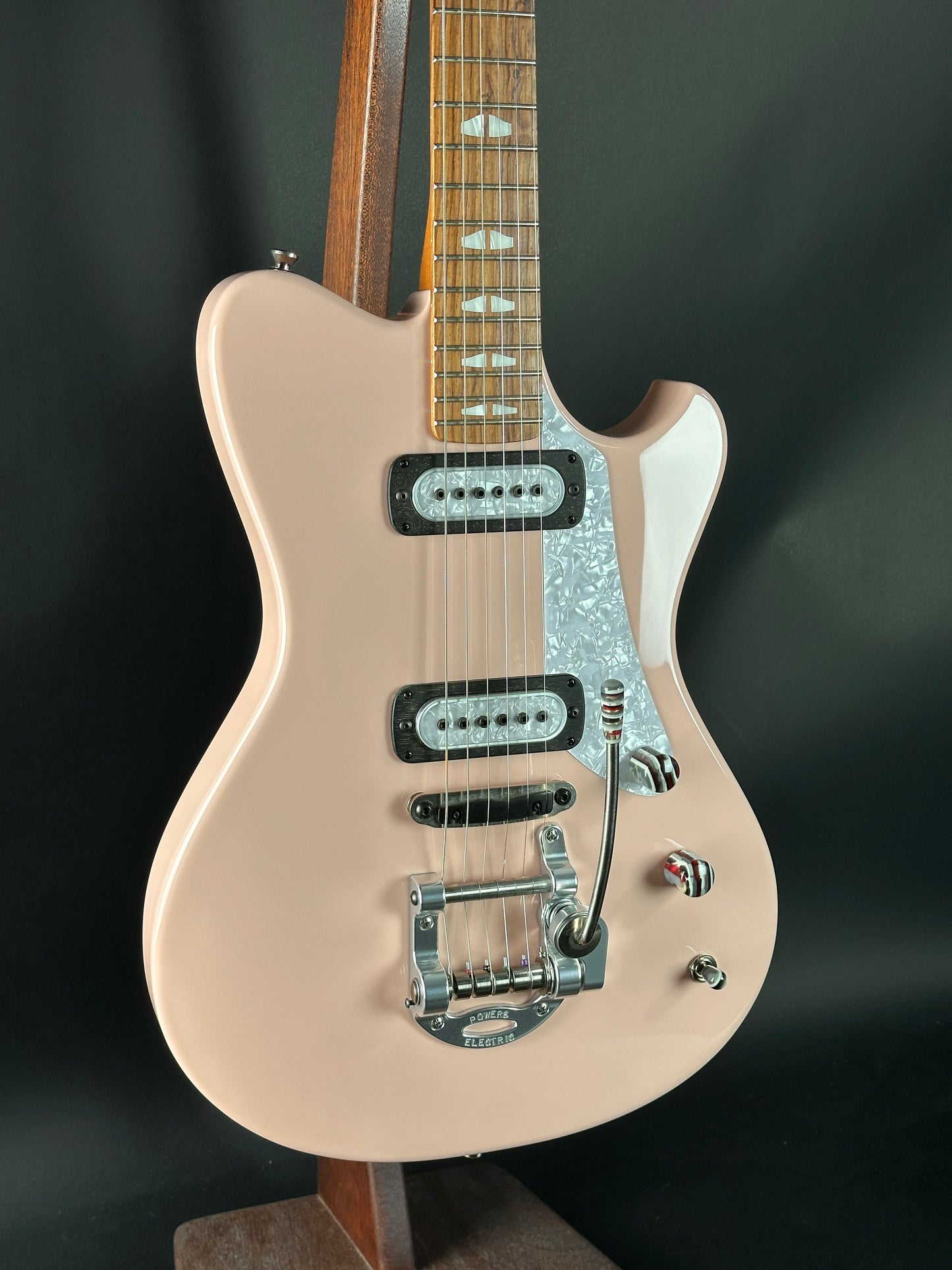 Beige electric guitar on a stand against a dark background