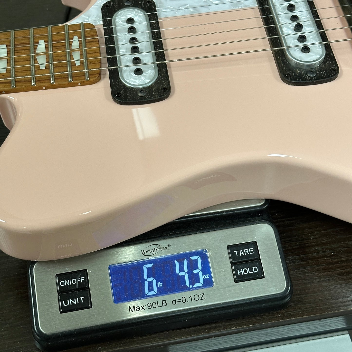 Beige electric guitar on a digital scale displaying weight.