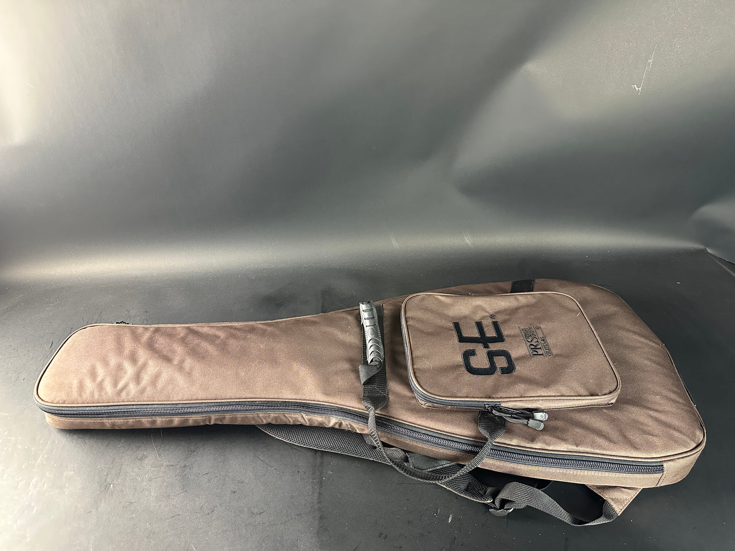 Beige guitar case with 'SE' branding on a gray surface