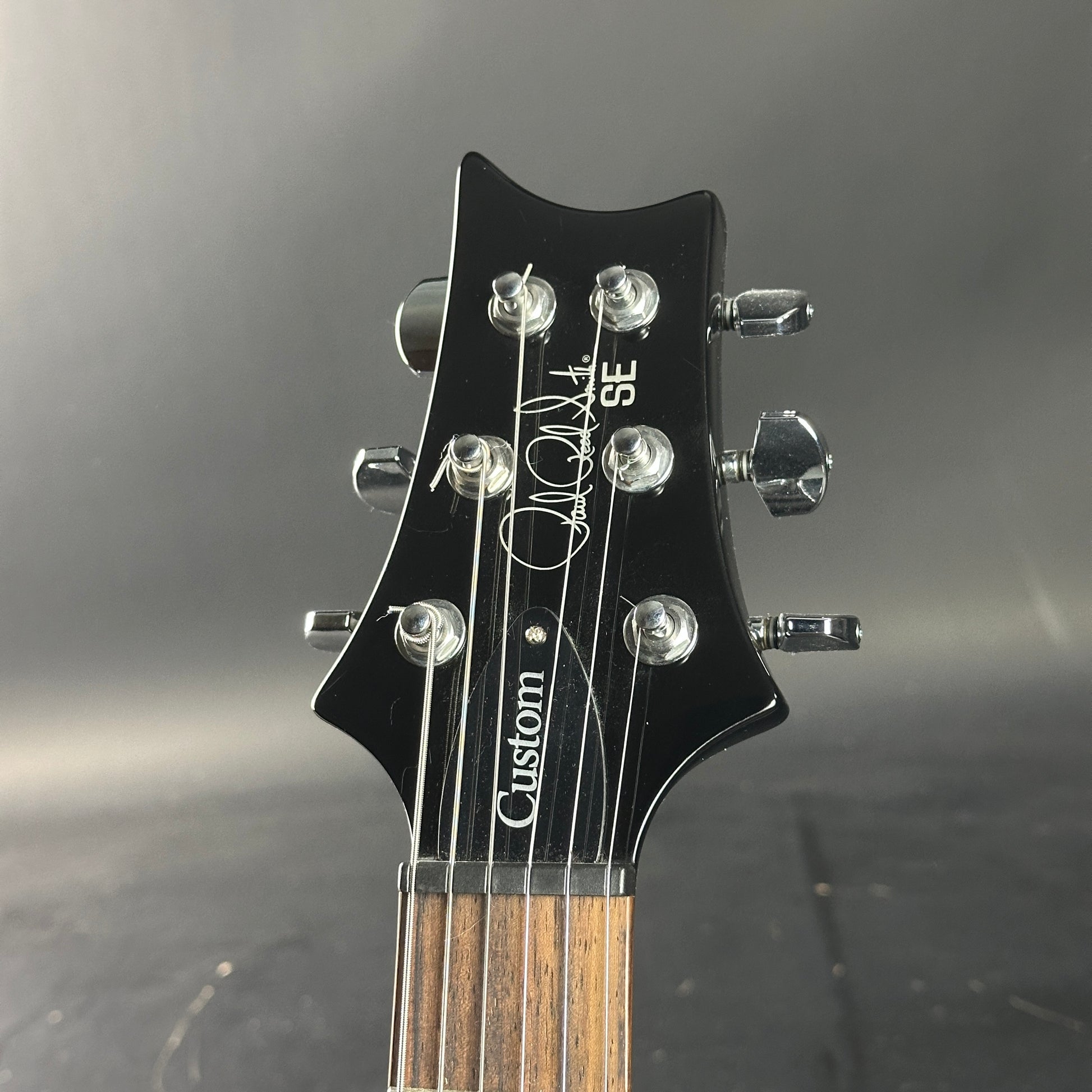 Guitar headstock with 'Custom SE' branding on a dark background