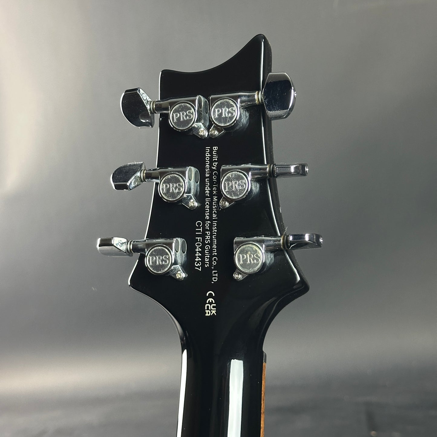 Close-up of a guitar headstock with PRS branding on a gray background