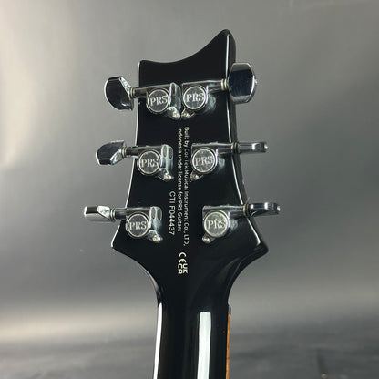 Close-up of a guitar headstock with PRS branding on a gray background