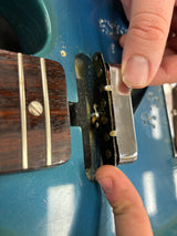 Person adjusting a guitar's tuners on a blue guitar body.