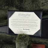 A close-up of a Martin Custom Shop Certificate of Authenticity card inside a black sleeve, placed on dark green fuzzy fabric with part of a brown Martin logo tag visible.
