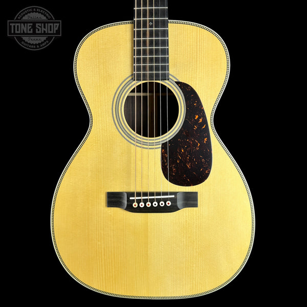 A front-facing acoustic guitar with a natural wood finish and dark tortoiseshell pickguard, shown against a solid black background with a Tone Shop watermark in the top-left corner.