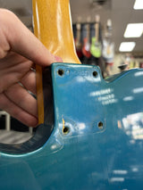 Close-up of a blue guitar with a person's hand holding the neck, in an indoor setting.