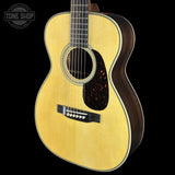 A natural wood acoustic guitar shown from a three-quarter angle against a solid black background, featuring a light yellow spruce top, dark brown sides, and a tortoiseshell pickguard.