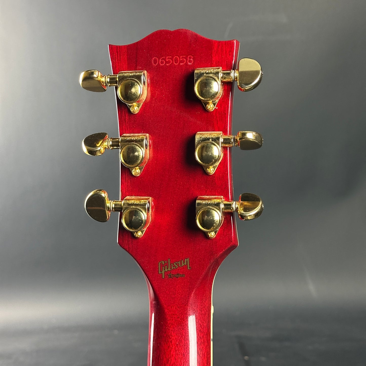Close-up of a red guitar headstock with gold tuning pegs on a gray background