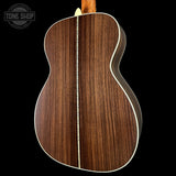 Close-up of the back of an acoustic guitar showing a rich dark brown wood grain finish with a light cream binding, set against a solid black background.