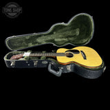 An acoustic guitar with a natural wood top and dark neck displayed inside an open black hard case with green plush lining, set against a solid black background. A 'TONE SHOP' watermark is visible in the top left corner.