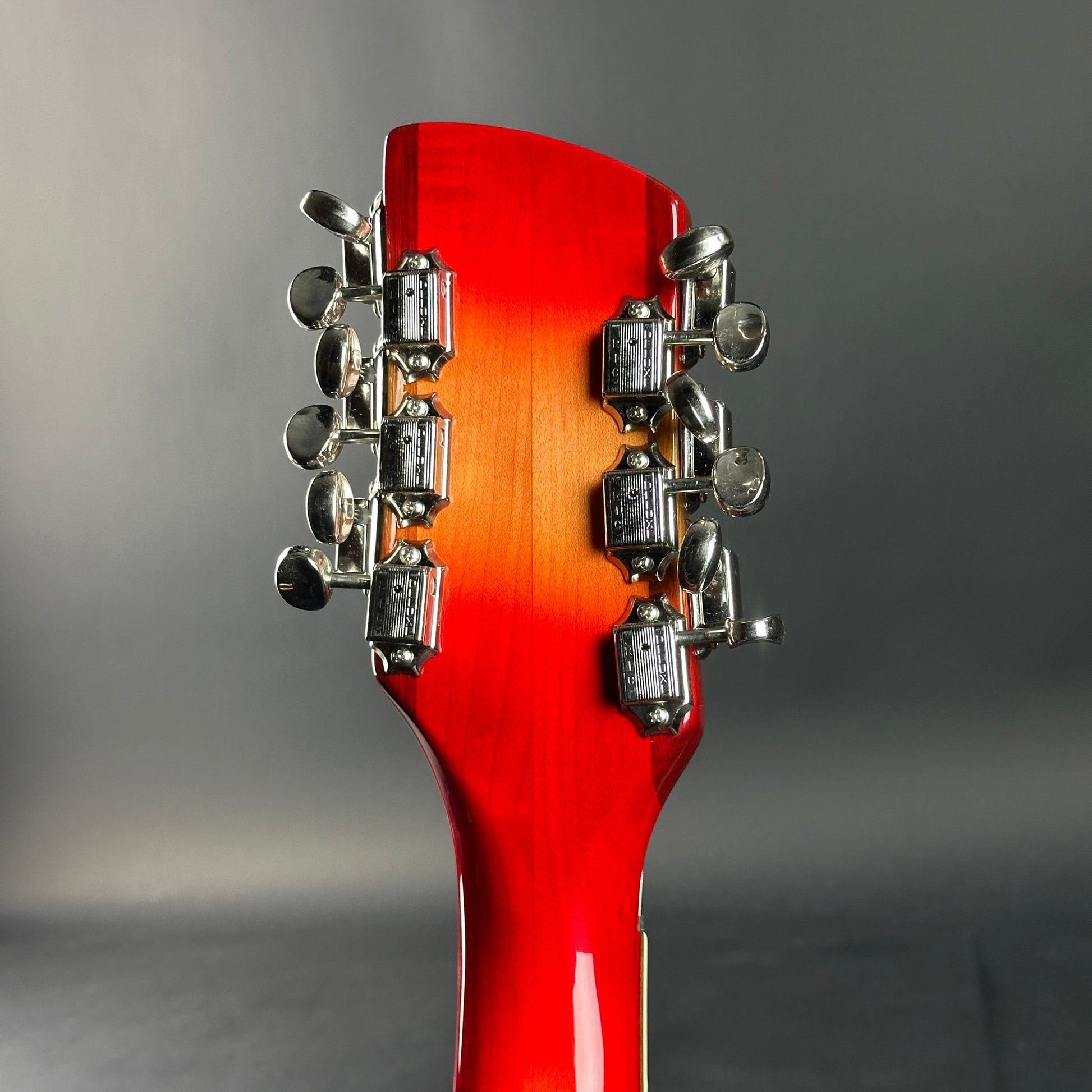 Close-up of a red guitar headstock with tuning pegs on a gray background