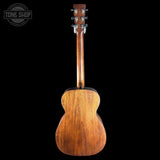 A wooden acoustic guitar shown from the back, featuring a glossy medium-brown wood finish and six silver tuning keys on the headstock, set against a solid black background with a Tone Shop watermark in the top-left corner.
