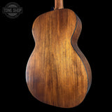 The back of a wooden acoustic guitar, showcasing a rich brown wood grain finish, set against a solid black background with a Tone Shop watermark in the top left corner.