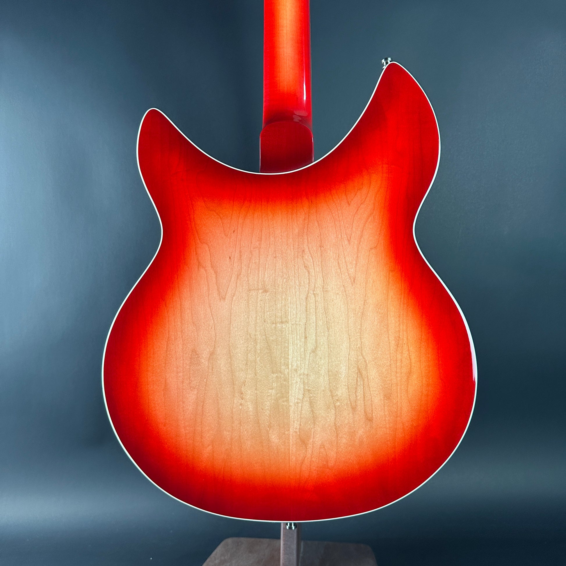 Red electric guitar body on a stand against a blue background