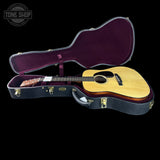 An acoustic guitar with a natural wood body and dark neck, displayed inside an open black hard case with a deep purple velvet interior. The Tone Shop logo is visible in the top-left corner.