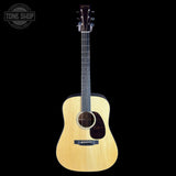 A natural wood acoustic guitar with a dark headstock, shown vertically against a solid black background. A circular 'TONE SHOP' watermark is visible in the top-left corner.