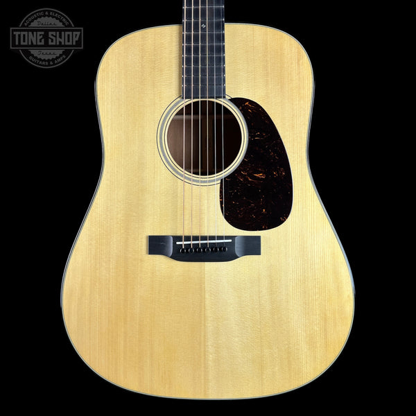 A front-facing acoustic guitar with a natural wood finish and dark pickguard, shown against a solid black background with a Tone Shop watermark in the top-left corner.