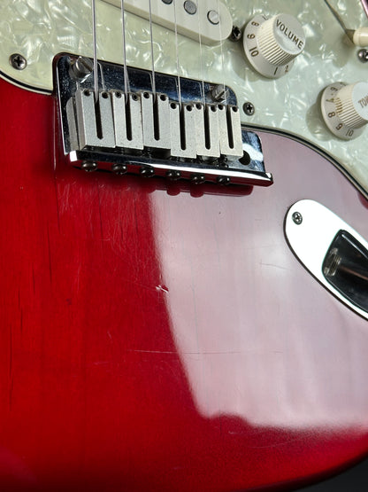 Close-up of a guitar's bridge and control knobs on a red electric guitar.