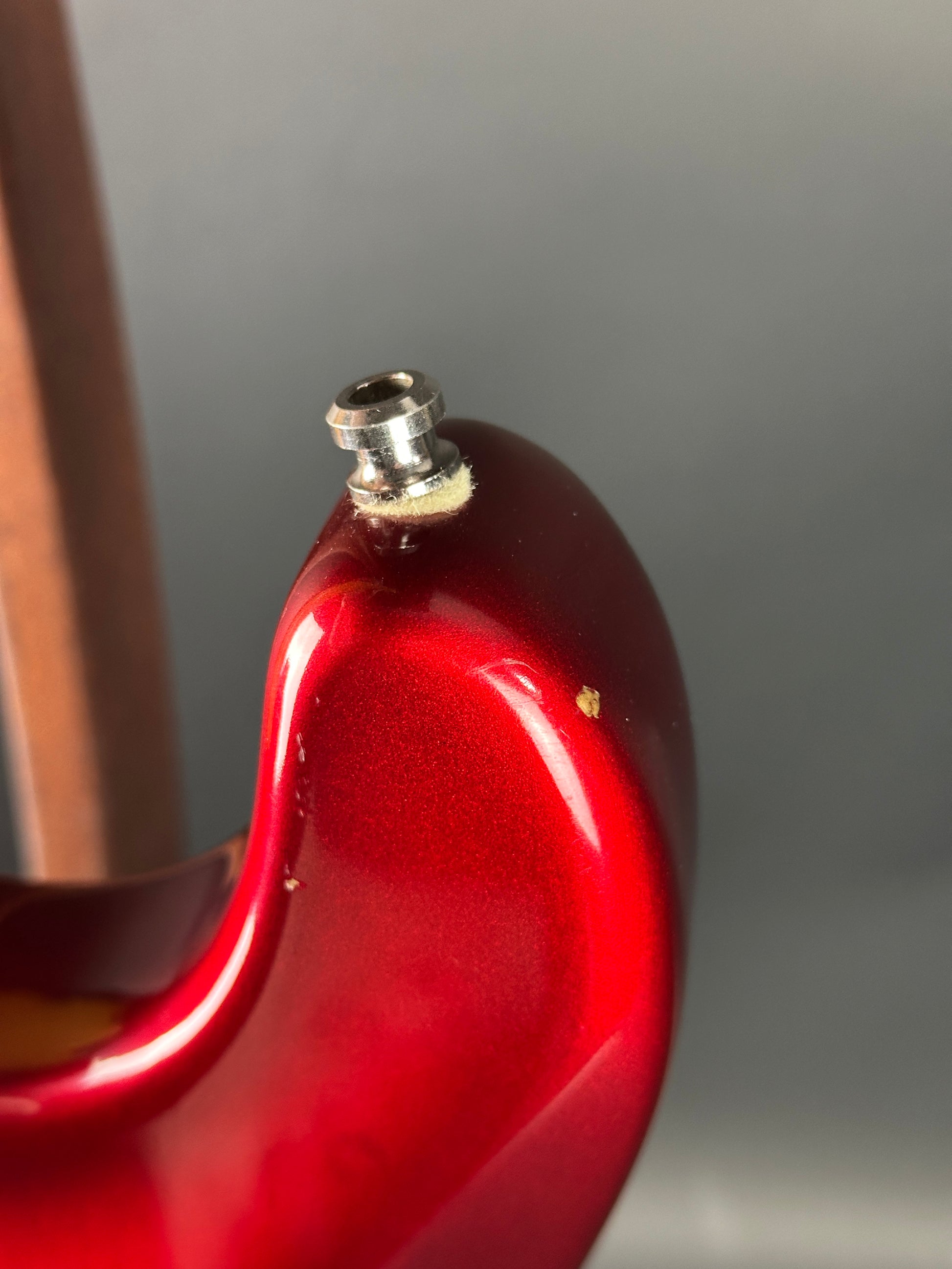 Close-up of a red guitar headstock with a tuning peg against a neutral background